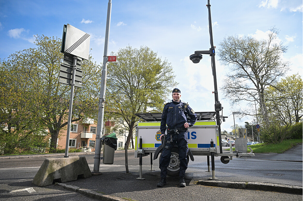 En polis står utomhus vid en rörlig kameravagn som används för kamerabevakning. Det är vår ute.
