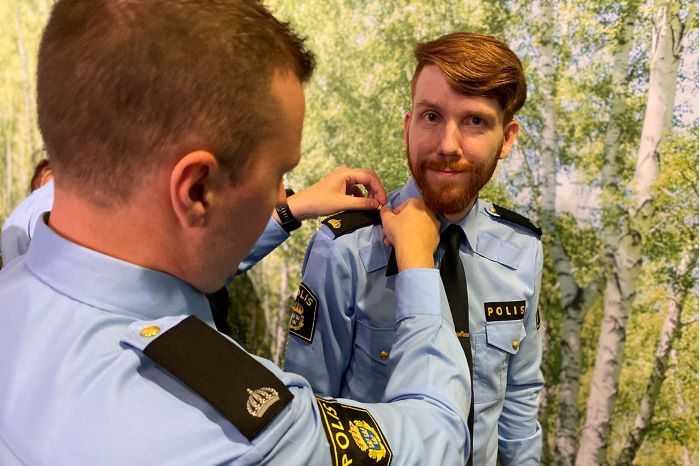 Två polisassistenter hjälper varandra att byta axelklaffar i deras uniformer.
