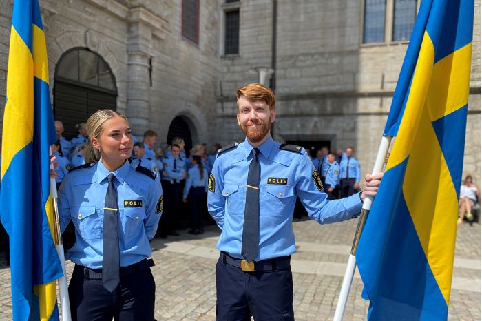 Två polisaspiranter som agerar fanbärare poserar med  svenska flaggan.