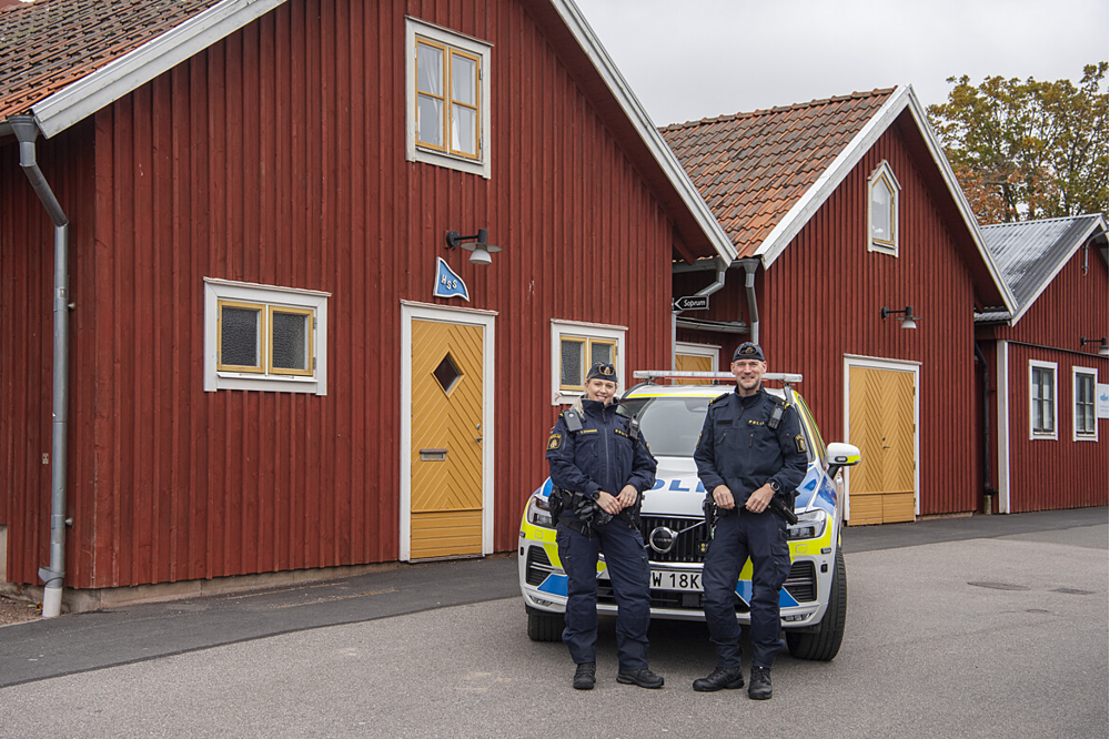 Två poliser som står framför ett rött hus och ler.