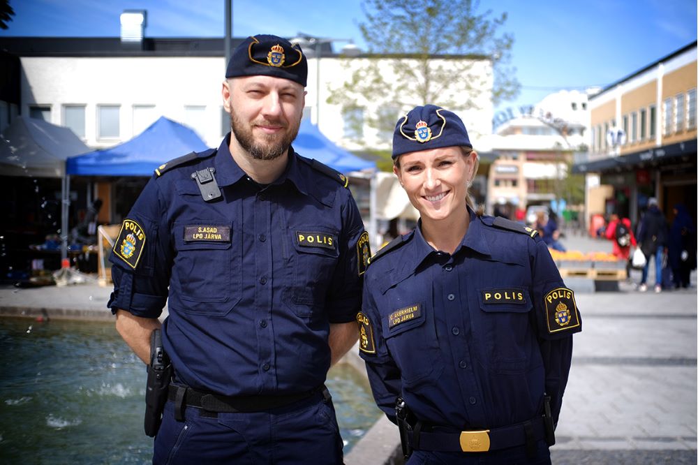 Två poliser i solsken framför fontänen på Rinkeby torg.