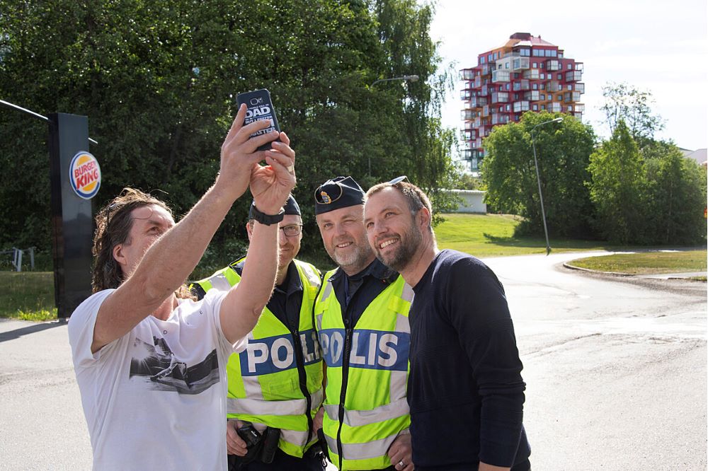 En person i vit tröja tar en selfie tillsammans med två uniformerade poliser