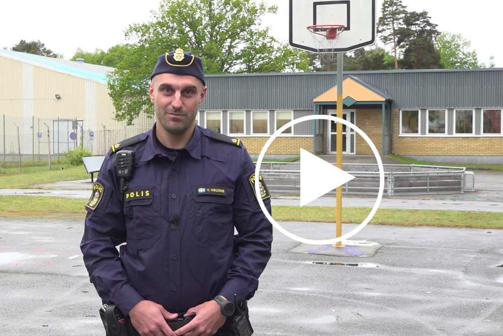 En polis på en skolgård i halvbild. Bredvid honom en vit grafisk play-knapp.