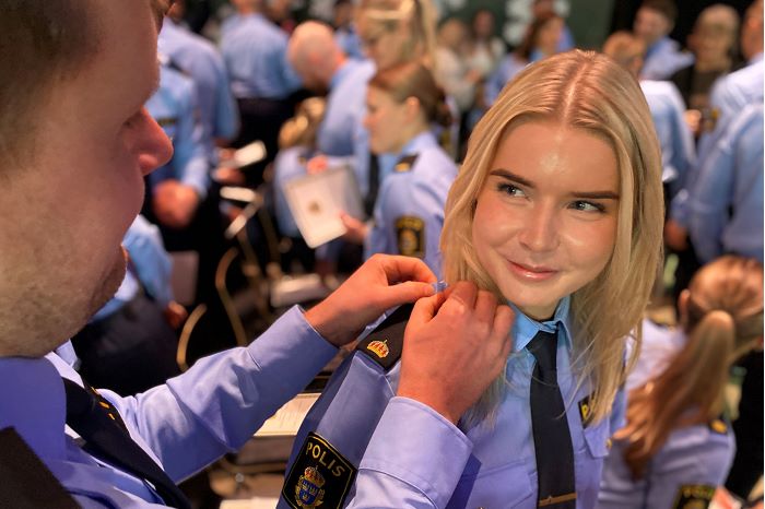 Fotografi som visar hur två polisassistenter hjälper varandra att byta axelklaffar.