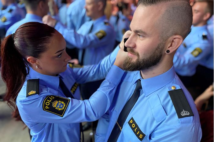 Fotografi som visar hur två polisassistenter hjälper varandra att byta axelklaffar.