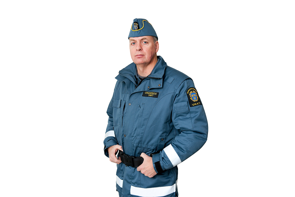 Båtmössa och jacka för ordningsvakter i blått med vita reflexband och svart bälte. Jackan har texten "ordningsvakt" vänstra delen av bröstet och riksvapnet på övre delen av ärmen.