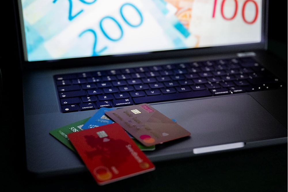 Bankkort som ligger på ett tangentbord, sedlar syns på datorskärmen
