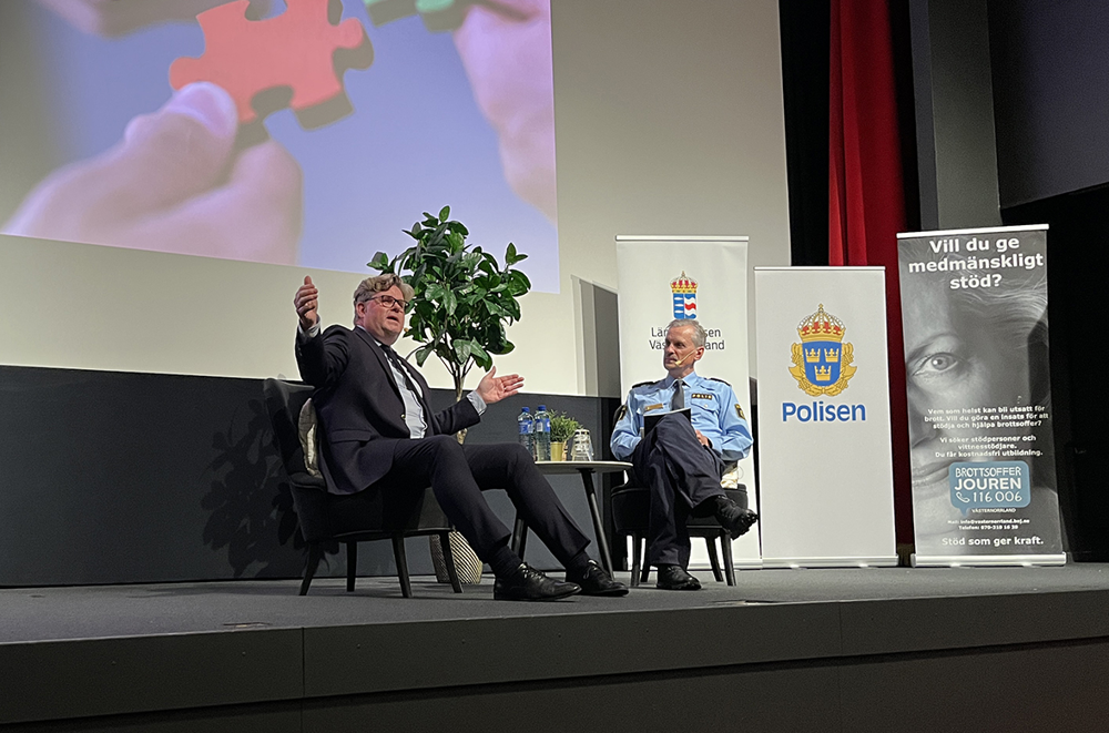 Två personer sitter i varsin fåtölj på en scen.