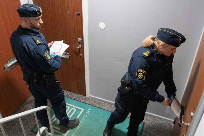 Foto på två poliser, en man och en kvinna, som lägger ner informationsblad i brev nedkastet.