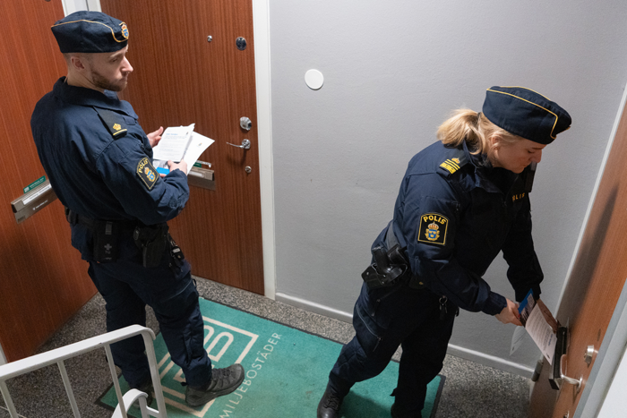 Foto på två poliser, en man och en kvinna, som lägger ner informationsblad i brev nedkastet.