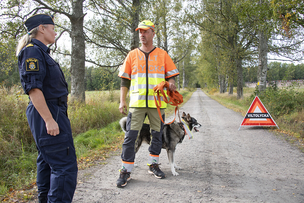 En kvinnlig polis pratar med en man med hund som eftersöker skadat vilt i skogen. 