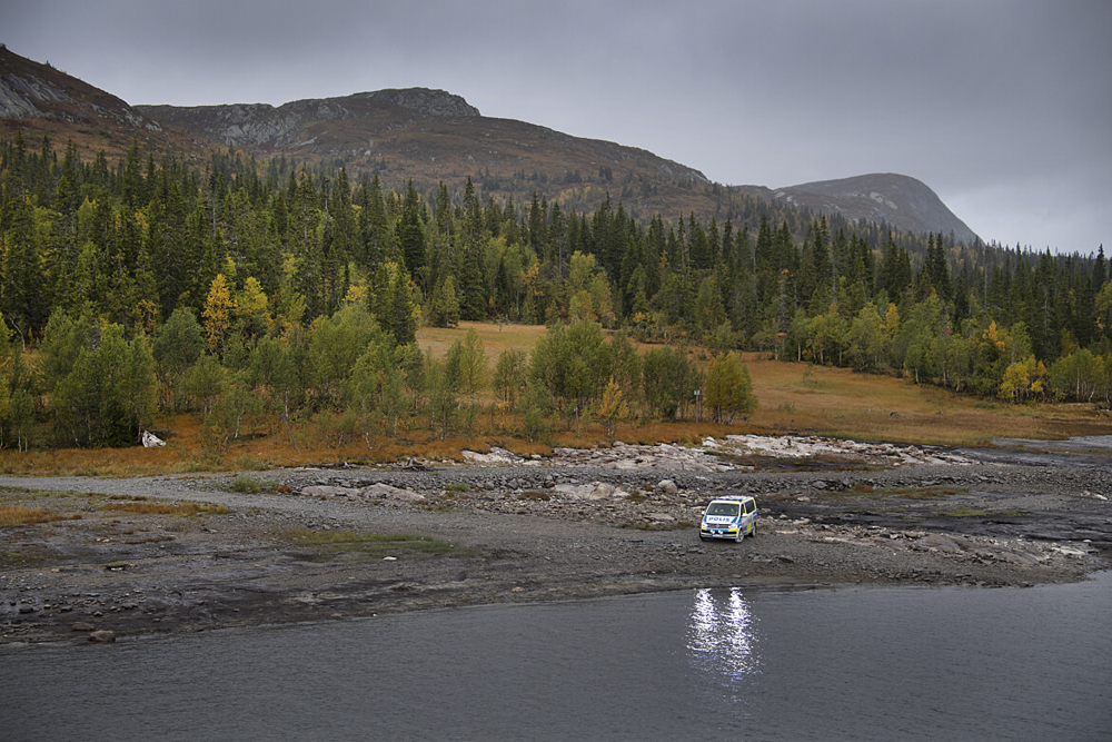 Naturbild med fjällen i Östersund, skogen, vattendrag och, på långt håll, en polisbil som är parkerad vid vattenbrynet