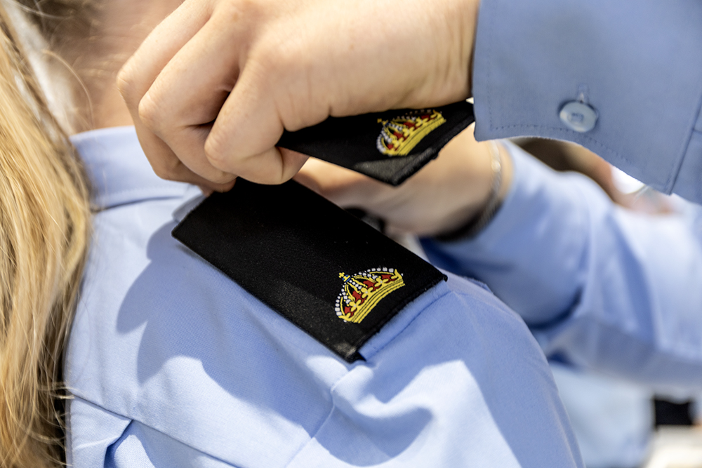 En hand byter en axelklaff. Den axelklaff som syns är en med guldigt emblem på en ljusblå polisskjorta.