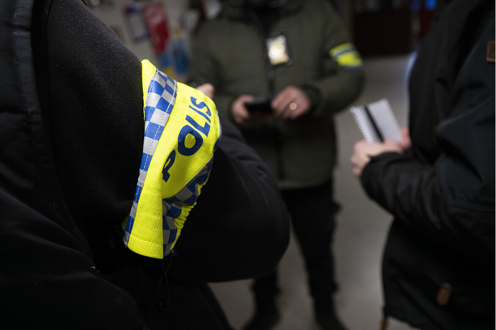Människor som pratar, civilklädda poliser och mörk miljö.