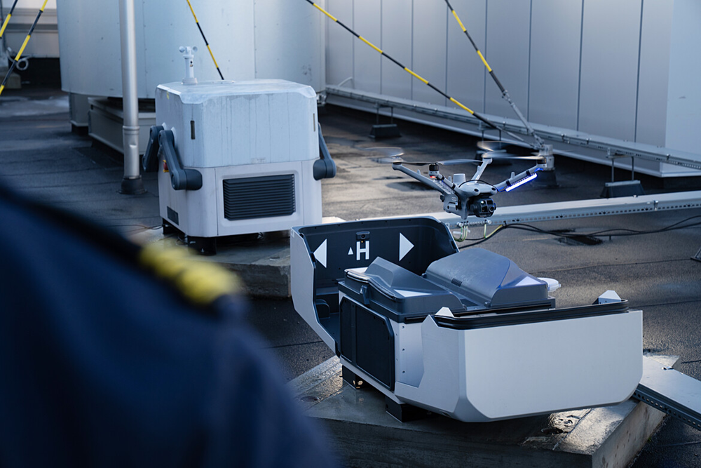 En drönare lyfter från marken. I förgrunden syns axeln på en uniformerad polis. 