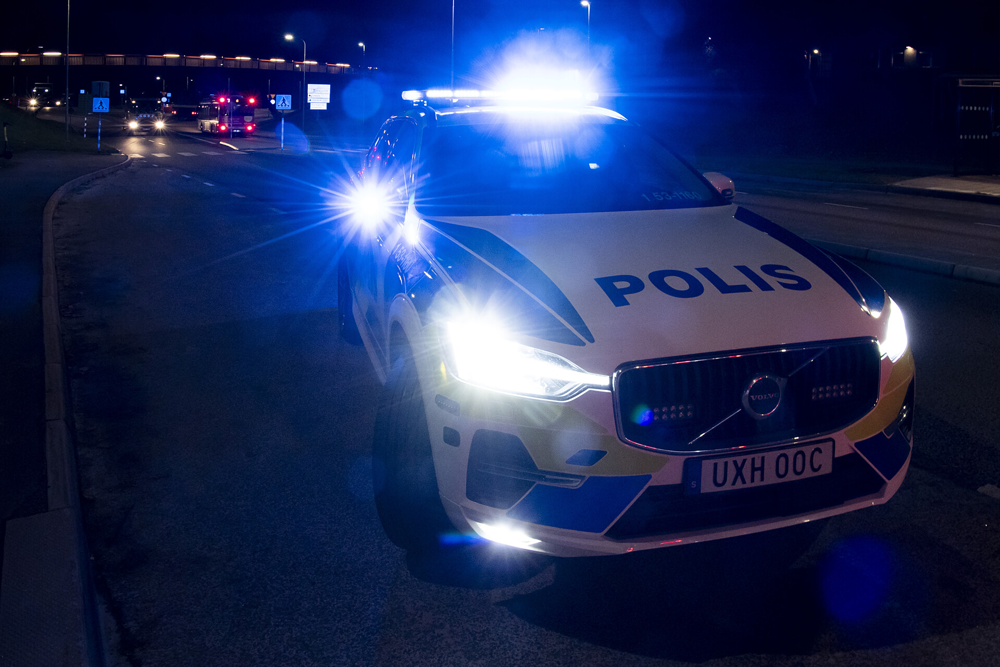 En polisbil står på en mörk gatan med blåljus tända