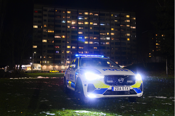 Polisbil i mörker framför lägenhetshus.