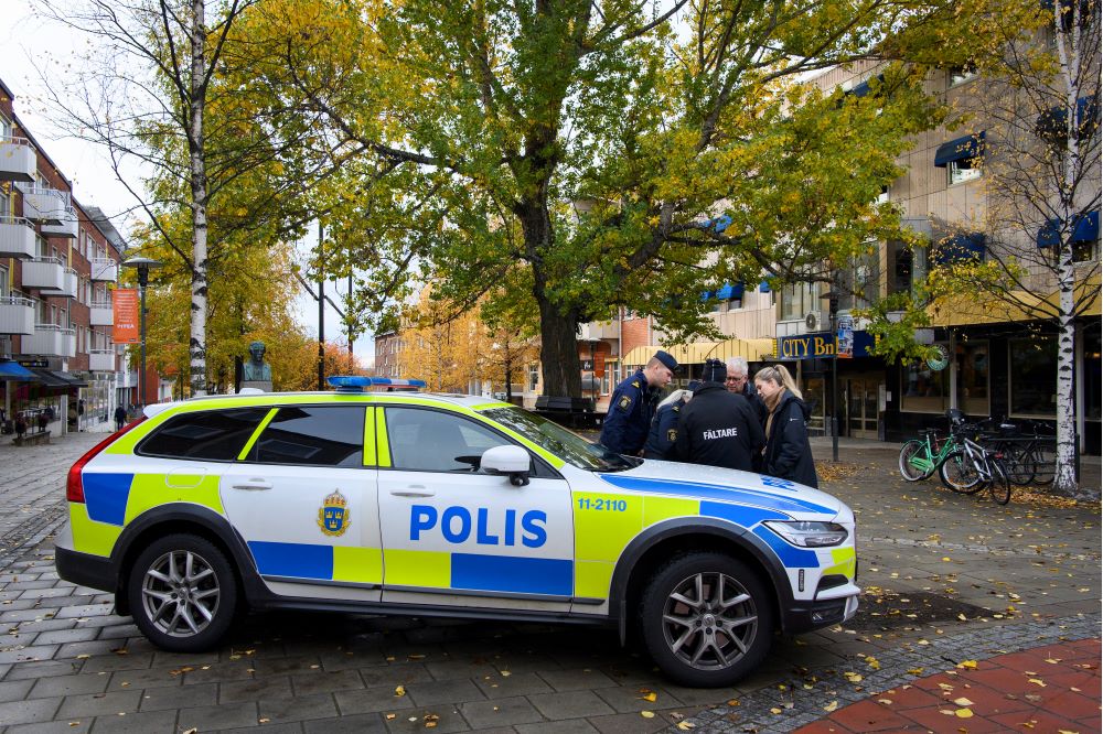 Polisbil parkerad i gatumiljö och poliser syns prata med någon utanför bilen