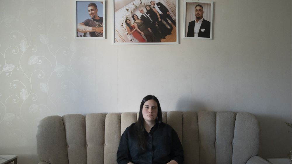 Foto på systern Frida som sitter på en soffa med bilder på sin bror bakom sig