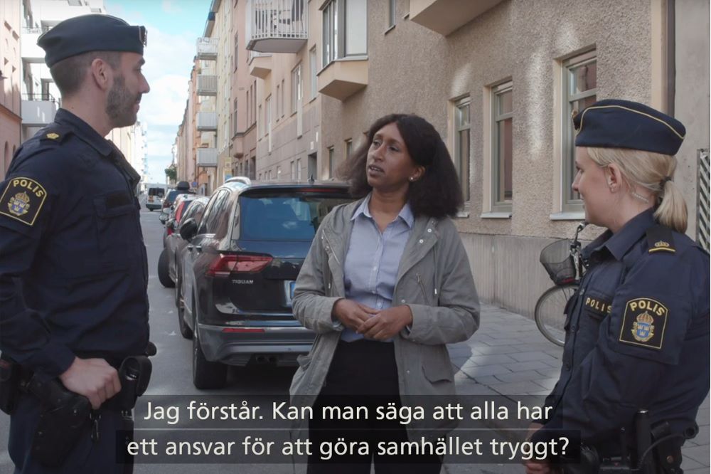 En kvinna står och pratar med två poliser på en gata.