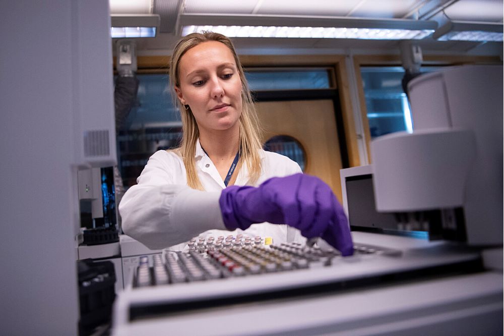 en person som bär en vit labbrock och lila skyddshandskar arbetar i laboratoriemiljö