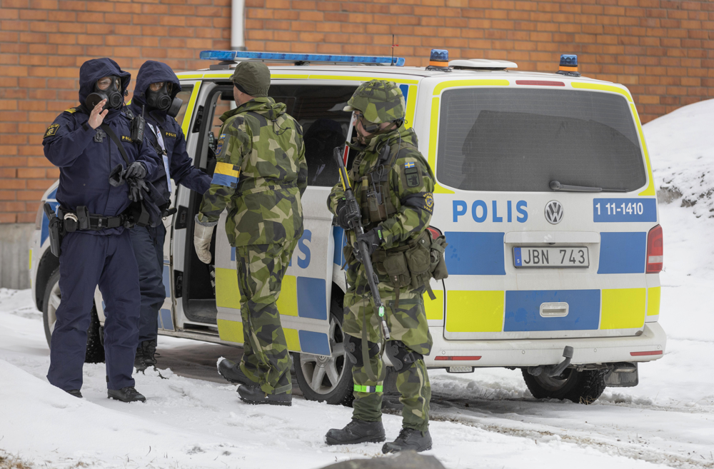 Bilden visar två poliser och två militärer i uniform som hälsar på varandra framför en polisbil.