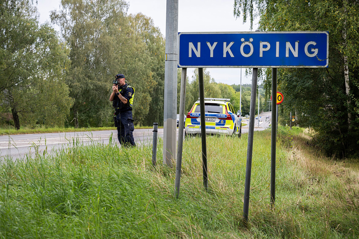 En polis genomför en hastighetskontroll. I förgrunden syns en ortskylt med texten "Nyköping".