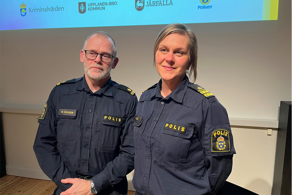 Foto på Magnus Nilsson och Frida Asp iklädda polisuniformer. Bakom dem visas en PowerPoint med loggor från kriminalvården, Upplands-Bro kommun, Järfälla kommun och Polismyndigheten.