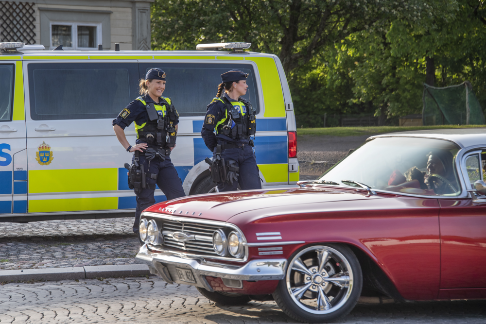 Två poliser med polisbil i bakgrunden och raggarbil i förgrunden
