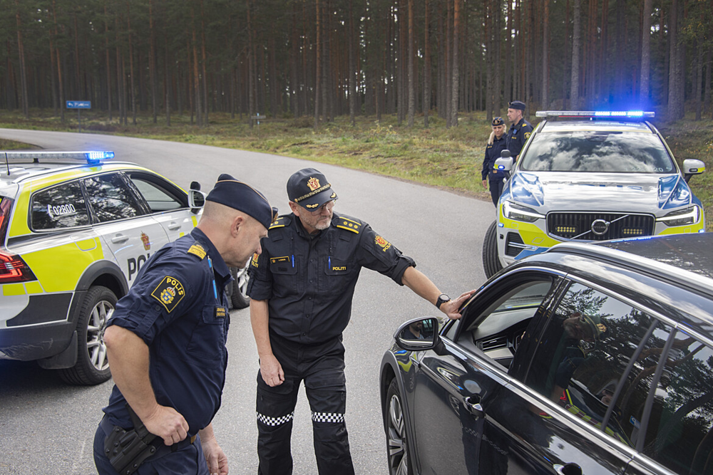 En svensk och en norsk polis i uniform stoppar tillsammans ett fordon för fordonskontroll. I bakgrund syns en svensk och en norsk polisbil.