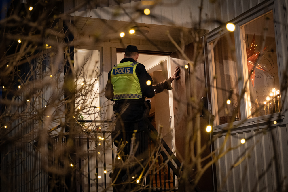 Foto på en polis i uniform som står vid ytterdörren av en villa och pratar med ägaren av huset.