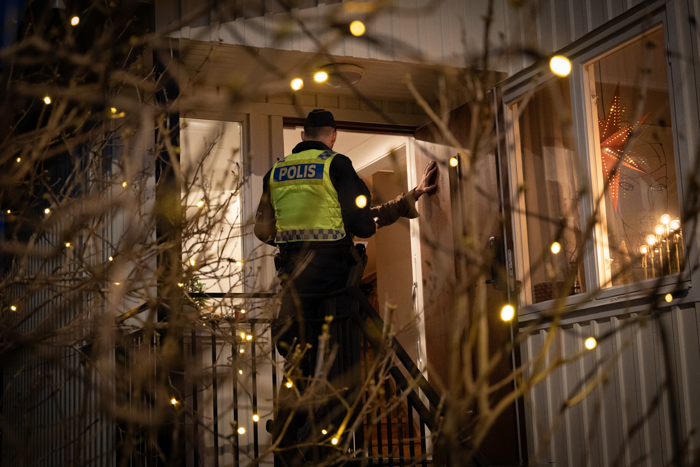 Foto på en polis i uniform som står vid ytterdörren av en villa och pratar med ägaren av huset.