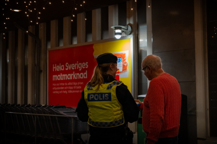 Foto på en polis i uniform som pratar med en medborgare utanför en matbutik.