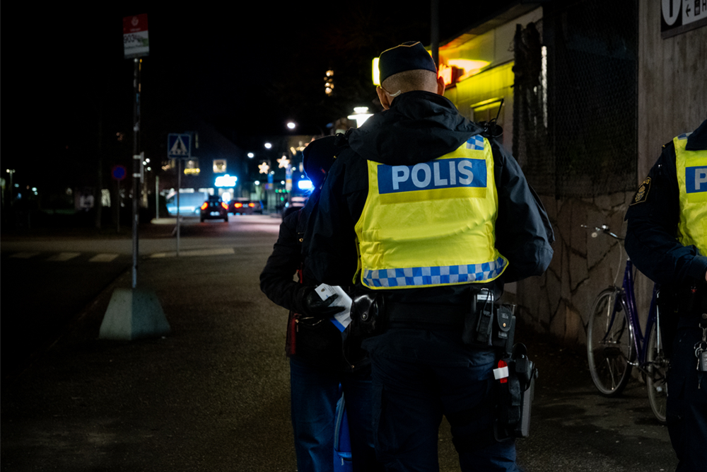 Foto på en polis i uniform som har ryggen mot kameran. Polisen pratar med en medborgare