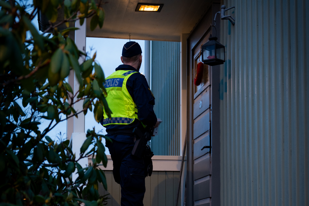 Foto på en polis i uniform som väntar på att någon ska öppna dörren vid en villa.
