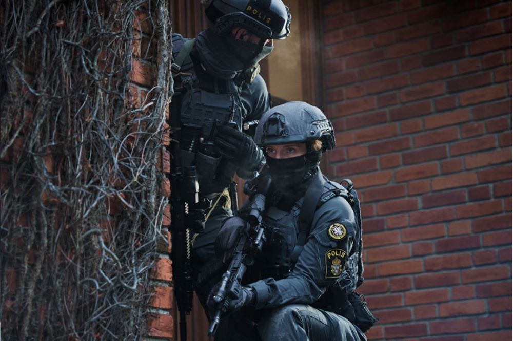 Skärmdump från filmen: insatspoliser spanar bakom en husvägg