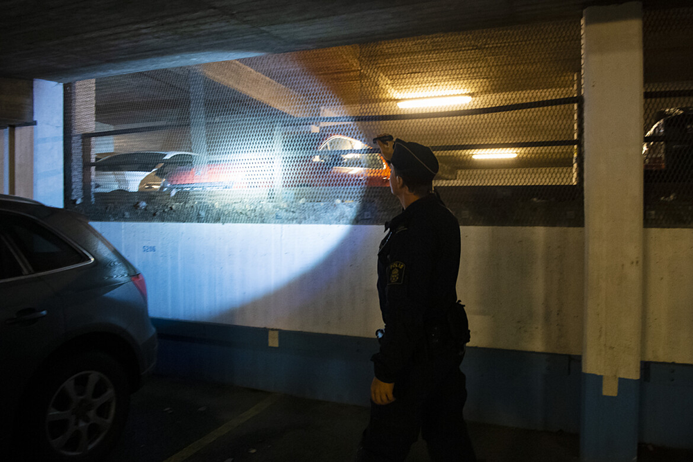 En polis genomsöker ett bilgarage med ficklampa. 