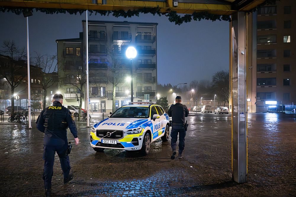 Två poliser bakifrån med en polisbil mellan sig. Det är mörkt ute.