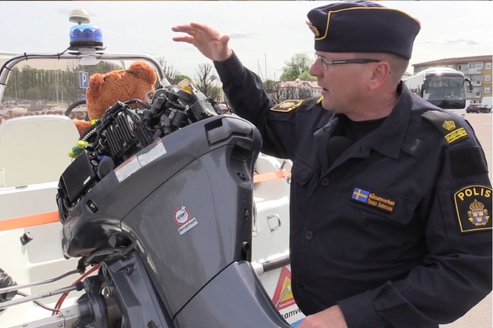 En polis såt bredvid en utombordsmotor som sitter på en båt.