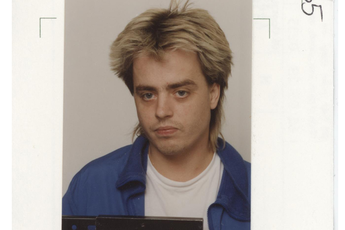 Foto på Peter Engström. På bilden har han längre hår, blont hår men håret intill hårbotten är något mörkare. Han har på sig en vit t-shirt och en mellanblå jacka.