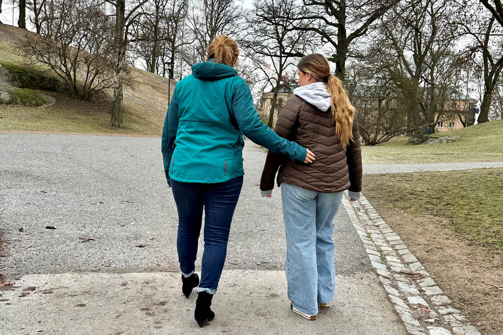 En vuxen kvinna och en tonårstjej går i en park