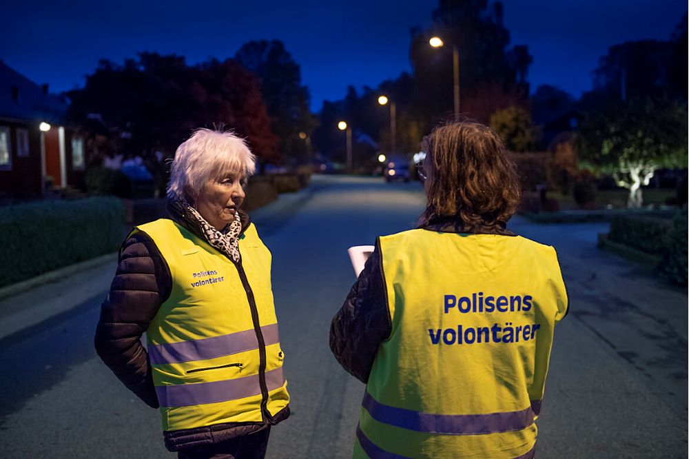Två volontärer med gula västar står och pratar på en gata nattetid.