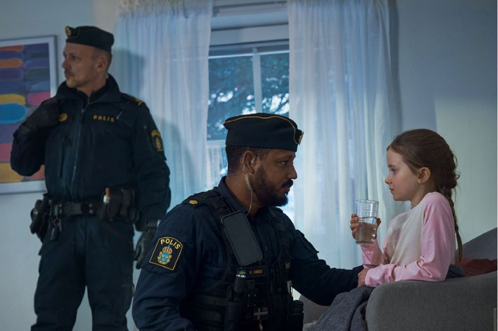 Skärmdump från film: två poliser, en av dem sitter och pratar med en liten flicka