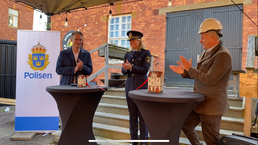 Polisområdeschefen markerar byggstart genom att klippa ett rött band som är knutet mellan två hus, ett stort och ett litet hus.