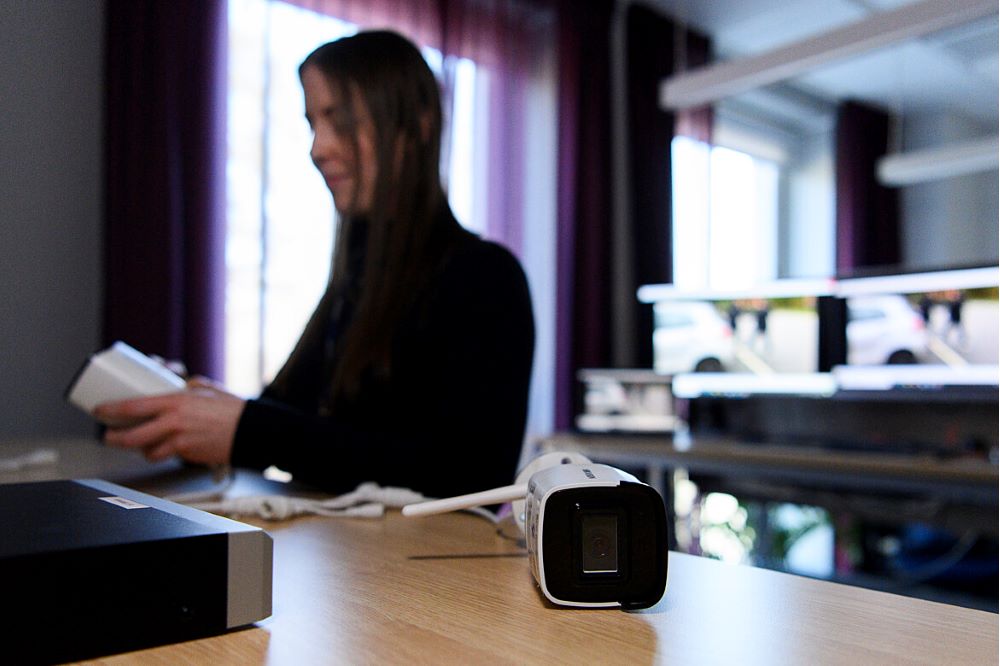 person sitter i en kontorsmiljö vid ett skrivbord med dator och annan teknisk utrustning