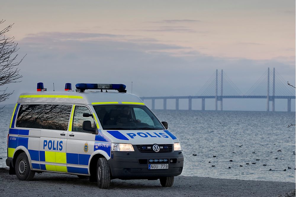Polisbil vid strand i Malmö med Öresundsbron i bakgrunden