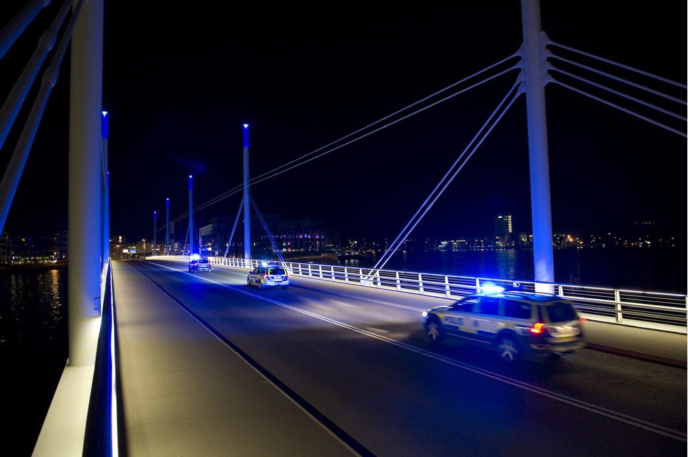 Fotografi som visar hur polisbilar nattetid kör med blåljus över Munksjöbron som samtidigt är upplyst med blå belysning.