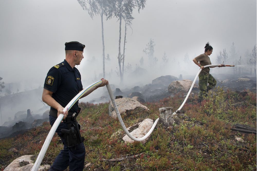 Polis och militär med brandslang släcker skogsbrand.