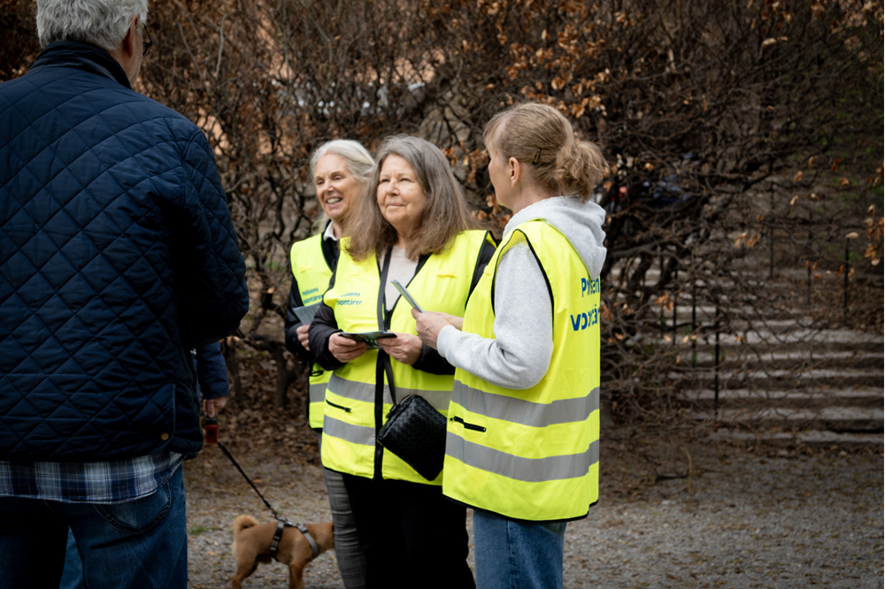 Tre av polisens volontärer pratar med män på en gata.