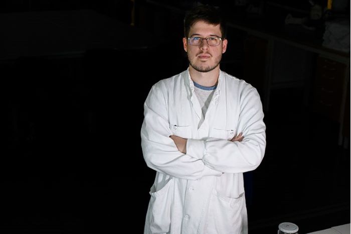 en man står i en mörk miljö, bär en vit labbrock